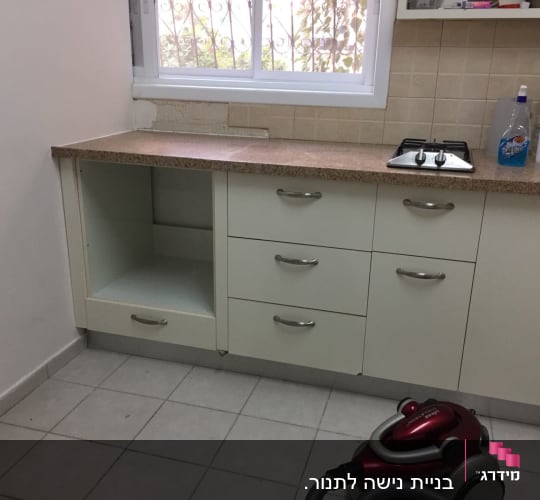 מטבח עם ארונות לבנים, כיריים ושואב אבק
